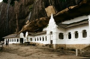 White architectural structure set against a rocky cliff with people exploring the site.