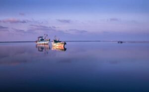 Calm waters and fishing boats under a pastel sky at sunset in Jaffna, Sri Lanka.